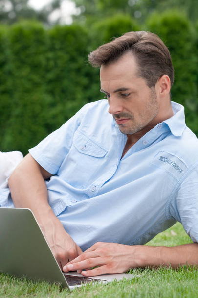 man using laptop while lying on grass - Photo, Image
