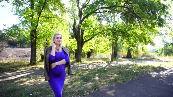 Jolie jeune fille blonde de façon familiale, posant pour la photographie, congelé et mettre une veste, se tient dans le parc sur fond d'arbres en plein air en journée
. - Séquence, vidéo