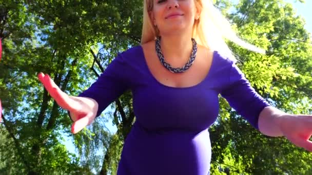 Потрясающая беременная девушка расправляет шары по сторонам улыбаясь и позируя прямо в камеру, стоя в зеленом парке на открытом воздухе днем
. - Кадры, видео