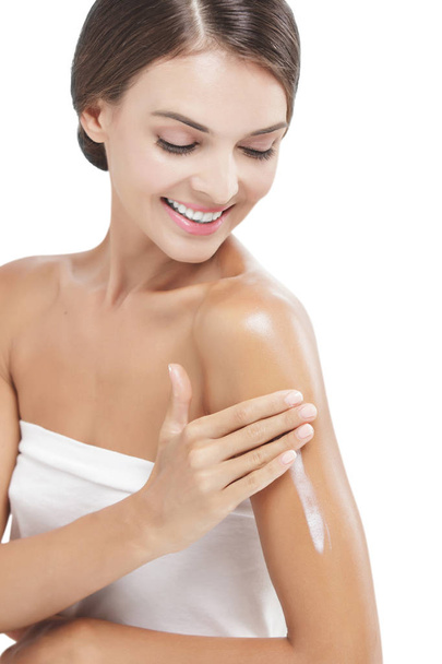 beautiful woman applying body lotion to her arms while smiling - Φωτογραφία, εικόνα