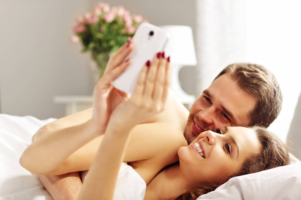 Giovane coppia a letto con smartphone
 - Foto, immagini