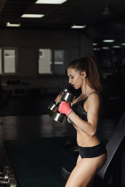 sexy Fitness-Frau in Sportbekleidung mit perfektem Fitness-Körper im Fitnessstudio, die Übungen mit der Hantel durchführt. - Foto, Bild