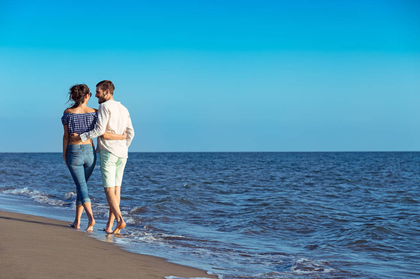 Happy interracial couple walking on beach. - Zdjęcie, obraz