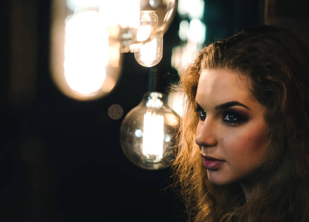 Portrait of a beautiful European girl. A woman stands near a wall surrounded by Edison's light bulbs. - Foto, immagini
