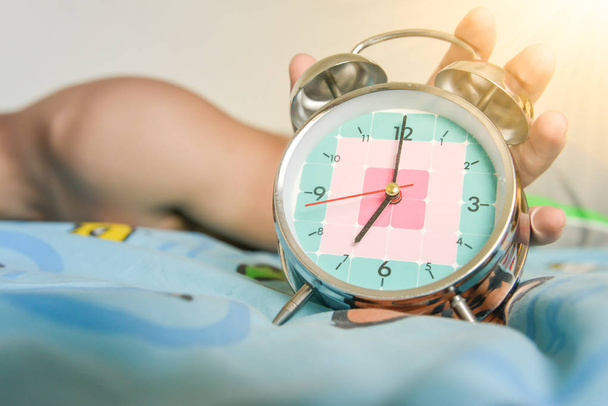 hombre somnoliento se está expandiendo la mano para detener el reloj despertador que muestra el tiempo para 7 AM
 - Foto, imagen