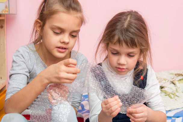 Twee meisjes gefascineerd bubbels barsten opblaasbare verpakking pakket - Foto, afbeelding