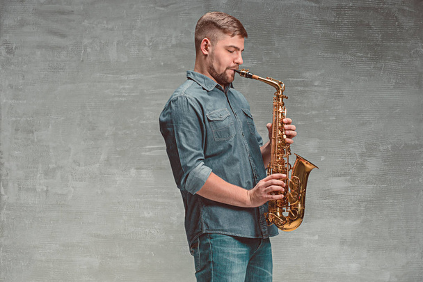 Happy saxophonist playing music on sax over gray background - Fotografie, Obrázek