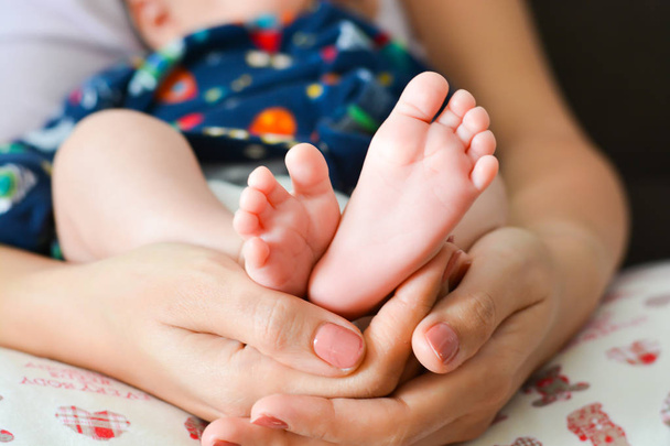 彼女の手のひらで生まれたばかりの赤ちゃんの足を保持している若い母親 - 写真・画像