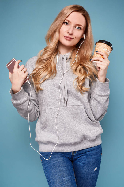 Linda mujer rubia positiva con capucha con teléfono y café
 - Foto, Imagen
