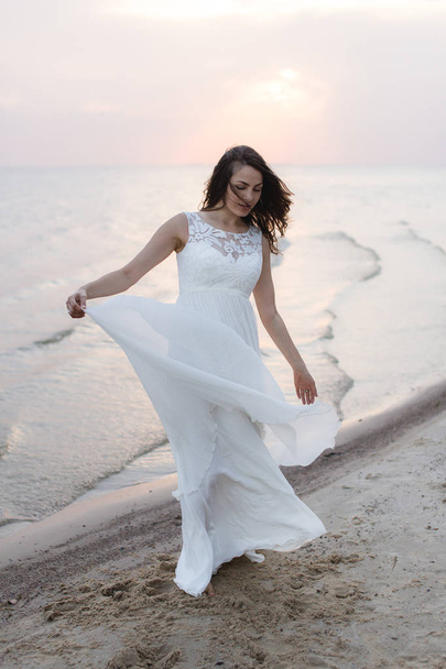 Beautiful young brunette woman in white long dress at the sea shore - Foto, immagini