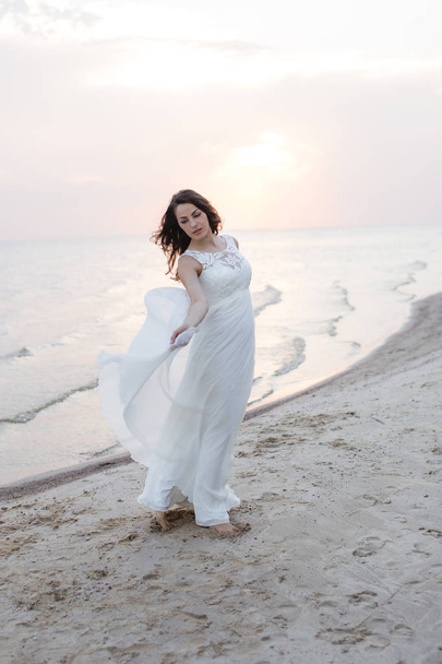Bella giovane donna bruna in abito lungo bianco sulla riva del mare
 - Foto, immagini