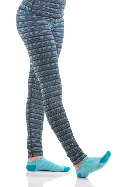 Nainen jalat venyttelyn aikana yllään värikäs sininen ja harmaa raidallinen urheilu housut ja sininen sukat
 - Valokuva, kuva