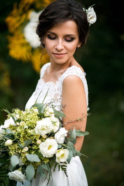 Portret van de mooie bruid in trouwjurk met een mooi boeket bloemen - Foto, afbeelding