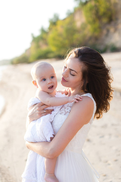 Mladá matka drží dítě v náručí na pláži u moře - Fotografie, Obrázek