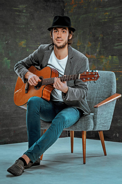 Cooler Typ mit Hut spielt Gitarre auf grauem Hintergrund - Foto, Bild