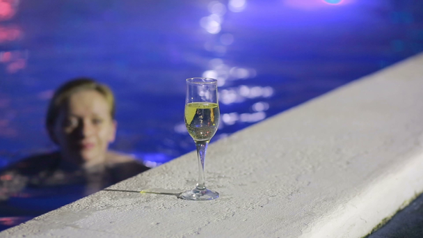 Kobieta w nocy w basenie z wodą termalną z lampką szampana - Materiał filmowy, wideo