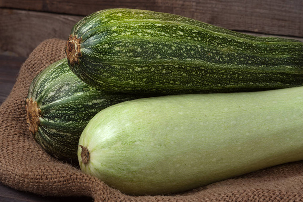 grüne Zucchini und Zucchini auf Sacktuch hölzernen Hintergrund - Foto, Bild