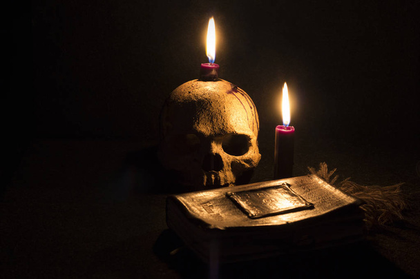 Μαύρο Magicskull και το κερί στο παλιό βιβλίο σε σκούρο χρώμα φόντου - Φωτογραφία, εικόνα
