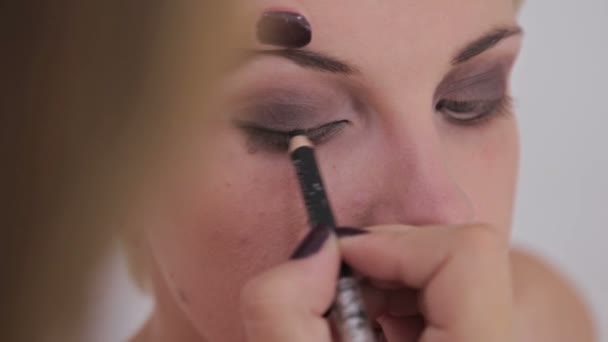 Close up shot. Make-up artist applying eyeliner around the entire eye of model - Felvétel, videó