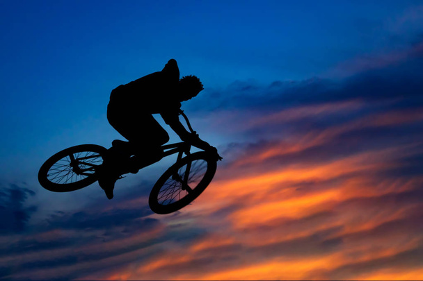 Σιλουέτα του ένας ποδηλάτης άλμα κατά τον όμορφο ουρανό στο sunse - Φωτογραφία, εικόνα