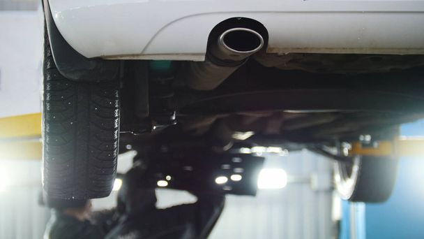 Servicio de coche - mecánico desenroscar el dispositivo de automóvil mientras trabaja bajo un tubo de escape levantado
 - Foto, imagen