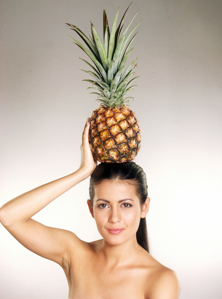 Young woman holding a pineapple over her head on white background - Фото, зображення
