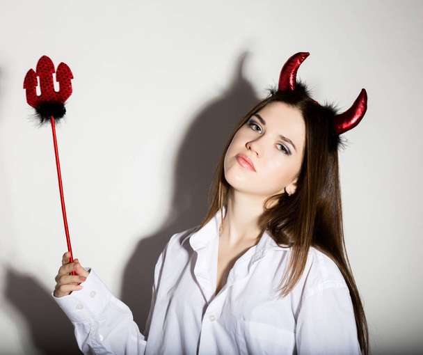 young girl in a mans white shirt with red horns looks like pretty Devil - Fotografie, Obrázek