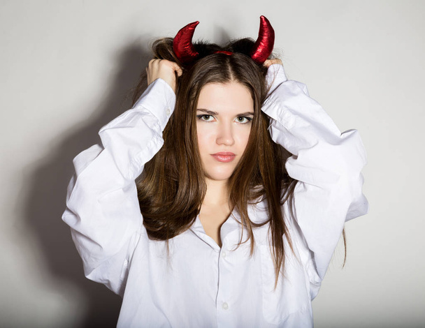 young girl in a mans white shirt with red horns looks like pretty Devil - 写真・画像