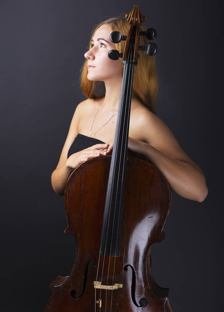 Menina bonita com um violoncelo no escuro. Violonchello. Menina com cabelos longos e lisos
 - Foto, Imagem