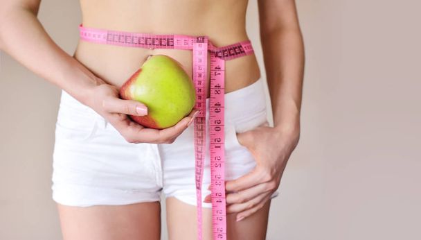 Mujer joven mide el cuerpo y sostiene la manzana
 - Foto, imagen