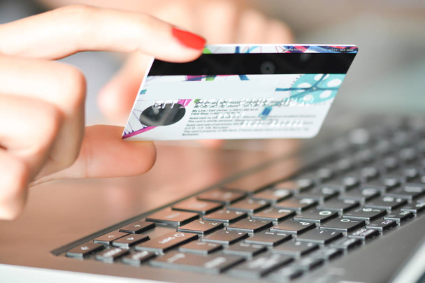Gros plan de la main d'une femme tenant une carte de crédit bleue à l'aide d'un ordinateur portable pour les achats en ligne
 - Photo, image