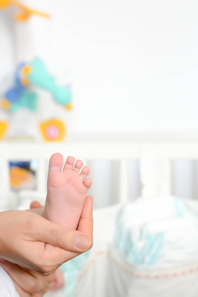 Νεαρή μητέρα κρατώντας το πόδι νεογέννητο μωρό στο τις παλάμες - Φωτογραφία, εικόνα