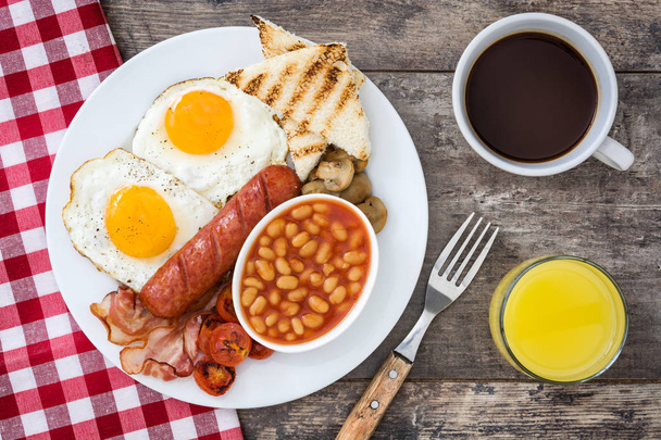 Tradycyjne pełne śniadanie angielskie z smażone jajka, kiełbaski, fasola, grzyby, pomidory z grilla i boczek na podłoże drewniane. Widok z góry - Zdjęcie, obraz