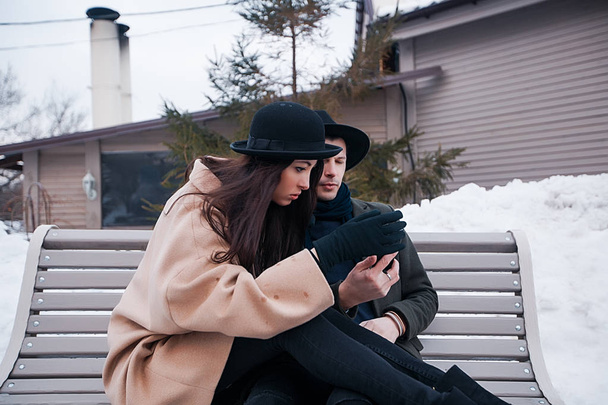  couple sitting on bench and looking at phone - Photo, Image