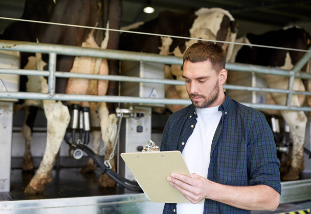 man with clipboard and milking cows on dairy farm - Zdjęcie, obraz