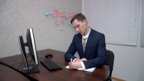 Young man making notes in his notebook in teh office - Video, Çekim