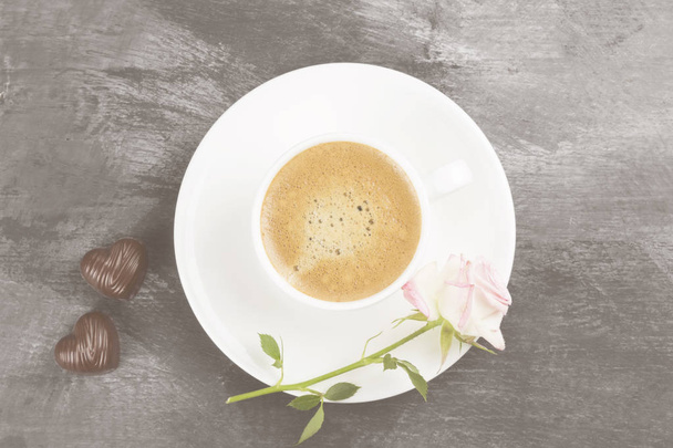 Espresso coffee in a white cup, a pink rose and chocolates on a dark background. Top view. Food background. Toning. - Foto, Imagen