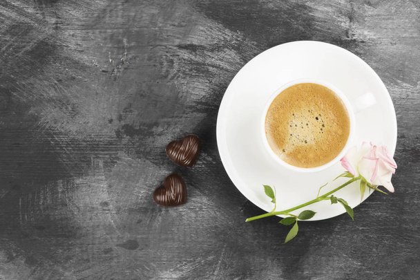 Espresso coffee in a white cup, a pink rose and chocolates on a dark background. Top view, copy space. Food background. - Foto, afbeelding