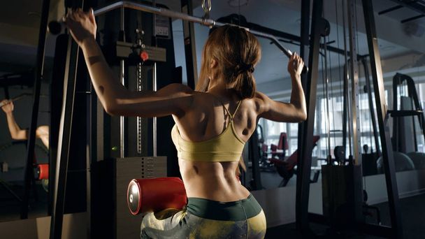Brunette in a gym flexing back muscles on aquipment. - Photo, image