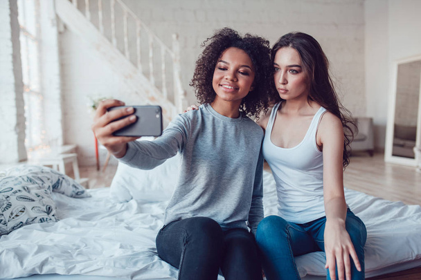 Beautiful girls make selfie sitting on bed at home. - Photo, Image