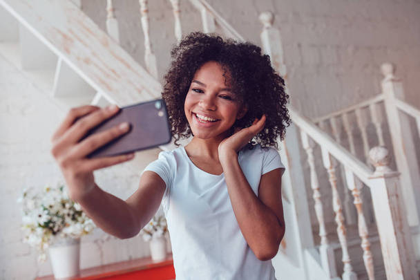 Beautyful african girl in white t-shirt make selfie using smartphone at home. - Photo, Image