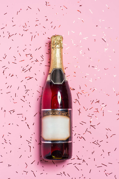 Flat lay of Celebration. Champagne bottle with colorful party streamers on pink background. - Fotó, kép