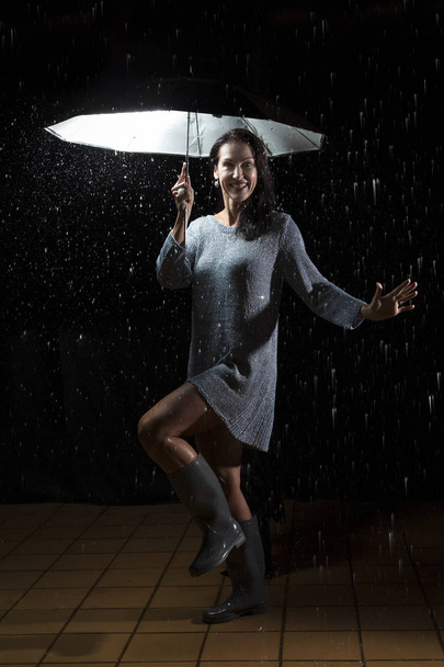 Beautiful woman with silver dress dancing in rain under an umbre - Photo, image