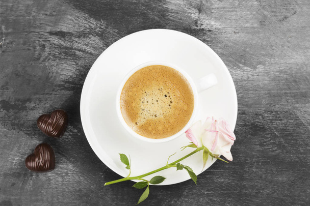 Espresso coffee in a white cup, a pink rose and chocolates on a dark background. Top view. Food background - Foto, imagen