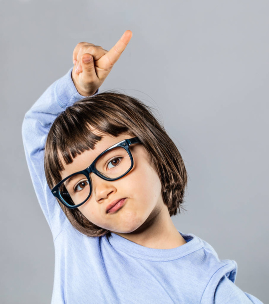 beautiful child with serious eyeglasses raising finger to answer question - 写真・画像