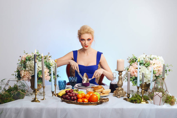 Fashion blonde model with colorful makeup sitting behind festive decorated table and cutting suede shoe - Foto, immagini