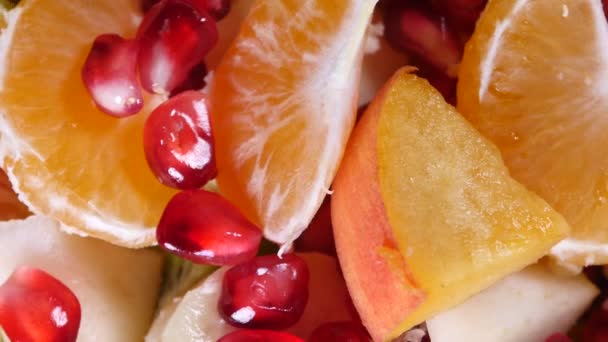 Top view of a fruit salad with mandarin, oranges, kiwi, pomegranate seeds, figs, banana and peaches - Footage, Video