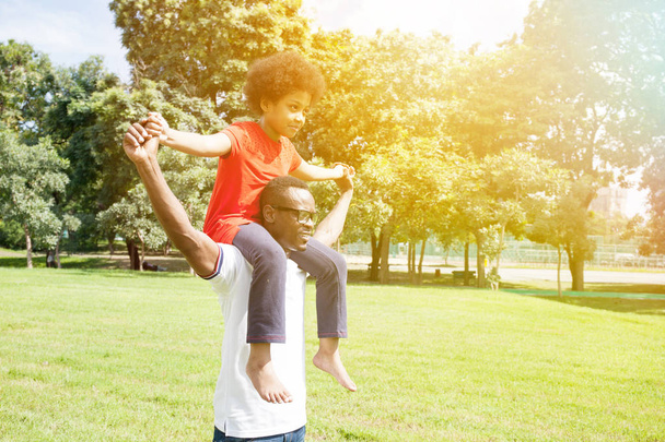 African American family doing piggyback and having fun in the outdoor park during summer - 写真・画像