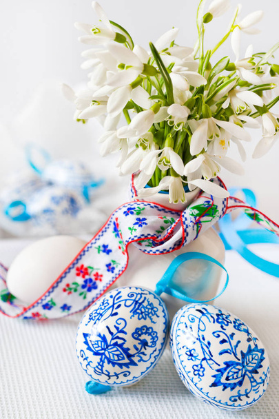 Traditional Czech easter decoration - flowerpot with white snowdrops flowers and decorated blue floral eggs on the white background. Spring easter holiday arrangement. - Photo, Image
