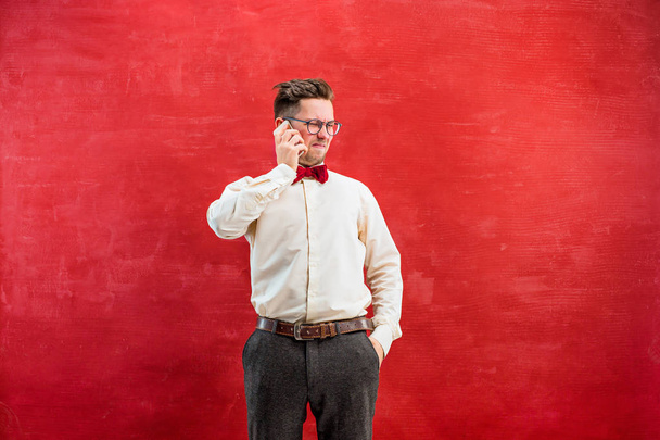 Portrait of puzzled man talking by phone a red background - Foto, Imagen